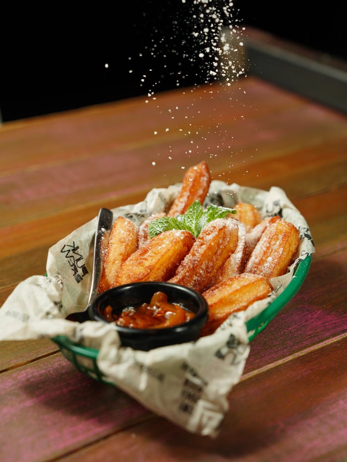 Close-up of freshly fried churros with sugar dusting and a chocolate dipping sauce on a wooden table.